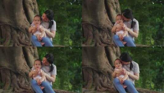公园里大树下妈妈抱着小宝宝玩耍高清在线视频素材下载