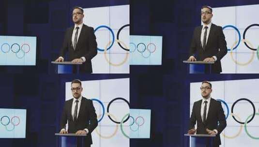 戴着眼镜站在领奖台后面举着奥林匹克旗阅读奥林匹克体育新闻的中年男性新闻主播高清在线视频素材下载