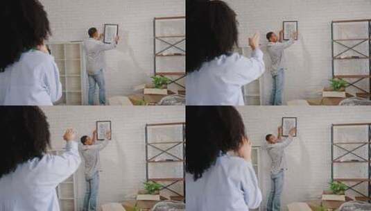 非洲裔美国年轻人在新公寓搬家时在墙上挂一幅画高清在线视频素材下载