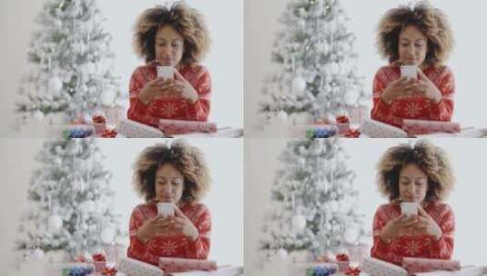 女子坐在圣诞树旁玩手机高清在线视频素材下载