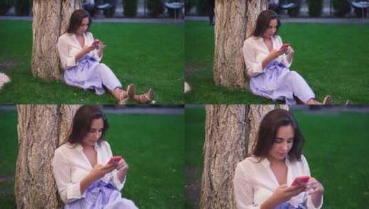 坐在公园树下的看手机的女人高清在线视频素材下载