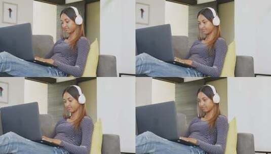 一个带着耳机的混血少女在家用笔记本电脑，慢动作高清在线视频素材下载