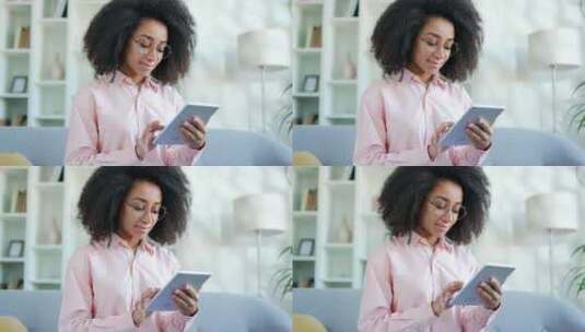戴眼镜的年轻非裔美国女性坐在家里客厅的沙高清在线视频素材下载