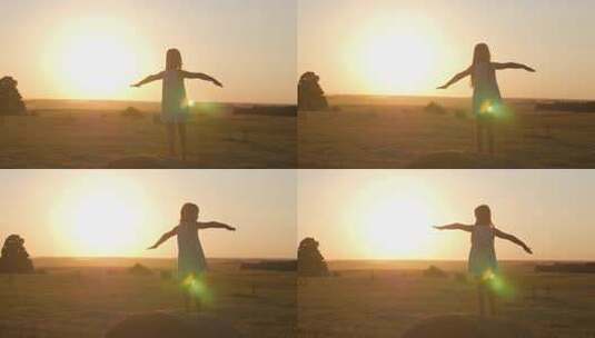 日落时，金色田野里的小女孩站在一卷稻草上，幸福地举起双手。美丽快乐的小女孩剪影在日落的天空中享受户外大自然。高清在线视频素材下载