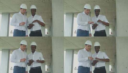 非裔美国工程师和高加索建筑师在建筑工地使用数字平板电脑并佩戴安全帽高清在线视频素材下载