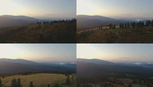 日出时，无人机在森林覆盖的山顶上向前飞行，远处雾蒙蒙的低地高清在线视频素材下载