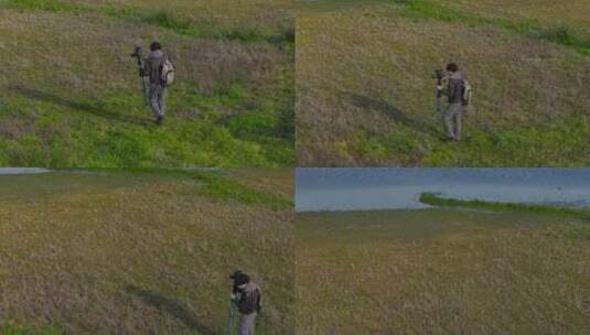 男摄影师在湖边的田野上用三脚架携带相机。高清在线视频素材下载