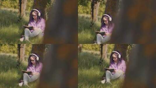戴眼镜耳机的年轻女子在夏天坐在树旁看书高清在线视频素材下载