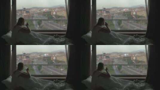 女人在床上喝咖啡，透过窗户看城市高清在线视频素材下载