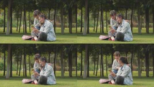 两位女大学生坐在校园草地上看手机学习交谈高清在线视频素材下载