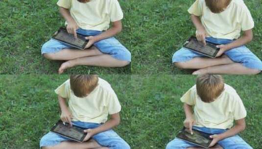 小男孩坐在草坪上玩平板高清在线视频素材下载