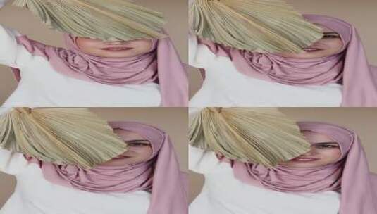 头戴粉色头巾的妇女用蒲扇掩住她的部分脸高清在线视频素材下载