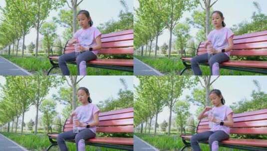 坐在公园长椅上喝水休息中国女孩高清在线视频素材下载