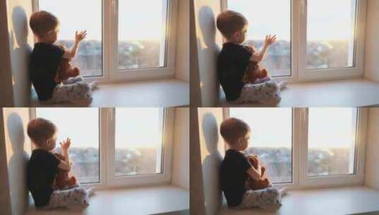 小男孩抱着小熊坐在窗户上，用手触摸阳光高清在线视频素材下载