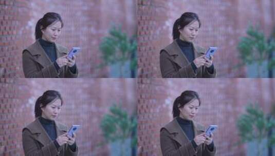 女性在红色砖墙前使用手机高清在线视频素材下载