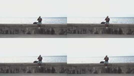 老人坐在海堤上吹小号高清在线视频素材下载