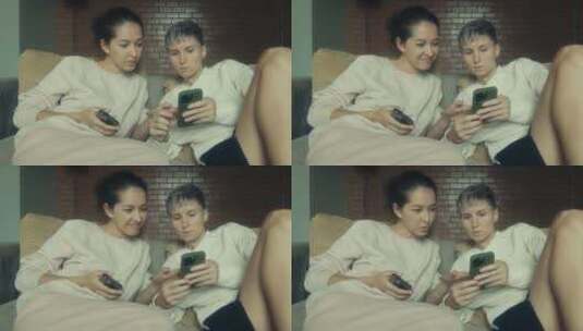 两个年轻女人拿着手机坐在家里的沙发上高清在线视频素材下载