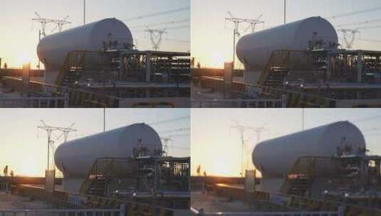 夕阳下高压电线塔附近巨大的储气罐航拍高清在线视频素材下载