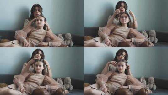 一位母亲坐在沙发上给十几岁的女儿做头发的高清在线视频素材下载