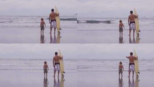 父亲拿着冲浪板和儿子站在海边高清在线视频素材下载