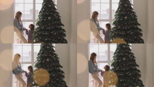 圣诞树前景上妈妈和女儿站在窗前牵手高清在线视频素材下载