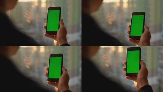 男性手持绿屏智能手机。站在窗户附近使用手机的男子。后视拍摄。色度键高清在线视频素材下载