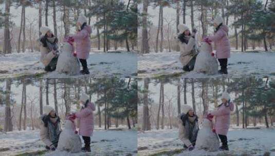 年轻妈妈和女儿在雪地里堆雪人高清在线视频素材下载