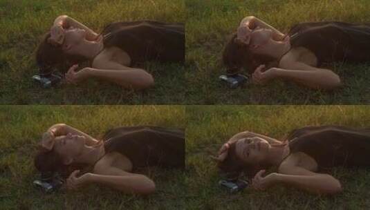 年轻女子躺在草地上，带着复古相机高清在线视频素材下载