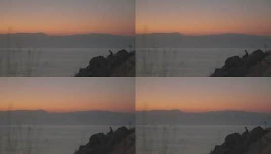 黄昏在海滩岩石上冥想的男人剪影高清在线视频素材下载