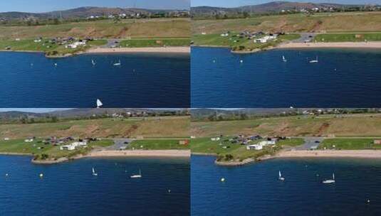 人们在湖边的帆船学校练习，那里有海滩、停车场和风力涡轮机高清在线视频素材下载