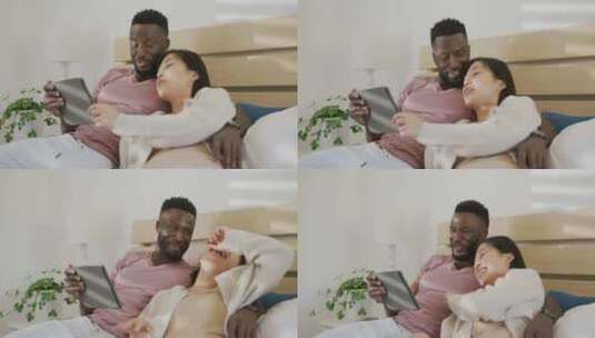 快乐的多样化夫妇使用平板电脑，躺在卧室里高清在线视频素材下载