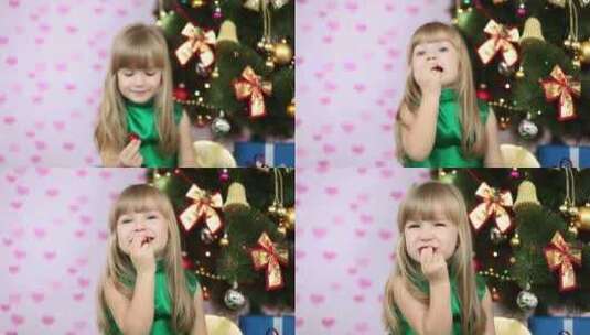 小女孩坐在圣诞树前吃糖果高清在线视频素材下载