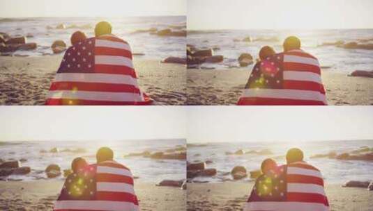 裹着美国国旗的夫妇坐在海滩上4k高清在线视频素材下载