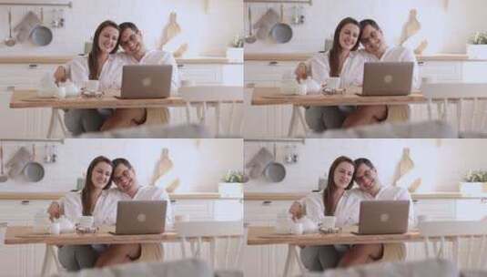 一对相爱的夫妇坐在家庭室spbi的桌子旁看着笔记本电脑屏幕聊天。年轻的男人和女人在电脑显示器上看网络或视频，微笑着交谈，拥抱，坐在灯光下的办公桌前高清在线视频素材下载