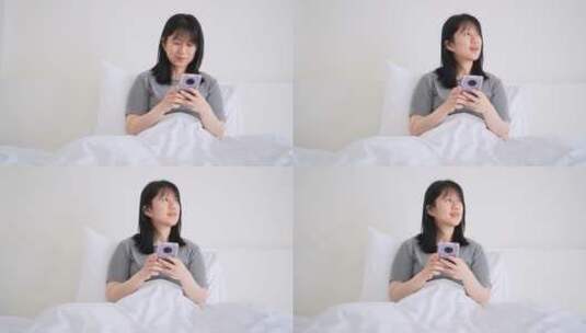 周末早晨年轻都市女孩懒在床上玩手机高清在线视频素材下载
