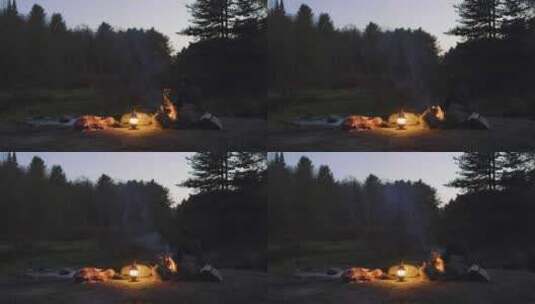 黄昏时分，一个人坐在森林里的篝火旁，手里高清在线视频素材下载