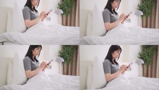 周末早晨年轻都市女孩懒在床上玩手机高清在线视频素材下载