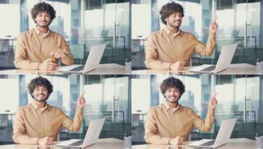 年轻微笑的男人坐在工作场所用手指指着写文高清在线视频素材下载