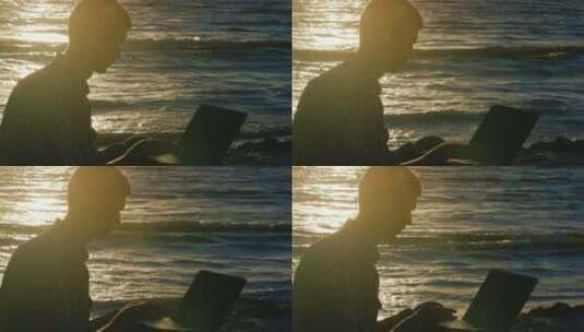 日落时分在海边用笔记本电脑工作的年轻人高清在线视频素材下载