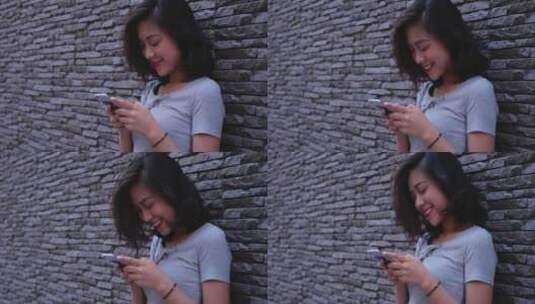 女孩靠着钻墙玩手机微笑高清在线视频素材下载