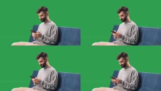 微笑的男人浏览互联网聊天社交网络沙发上的智能手机色度键绿屏高清在线视频素材下载