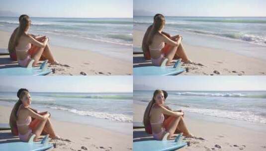 年轻的高加索女人坐在海滩的冲浪板上，对着高清在线视频素材下载