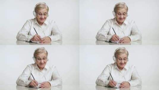 耳机里积极的老年女性在一张纸上写字的中景高清在线视频素材下载