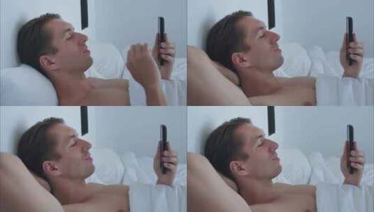快乐的男人一大早醒来，呆在床上在电话上输高清在线视频素材下载