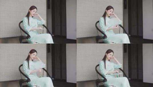 年轻旗袍女子摇着扇在中式合院门廊椅子休息高清在线视频素材下载