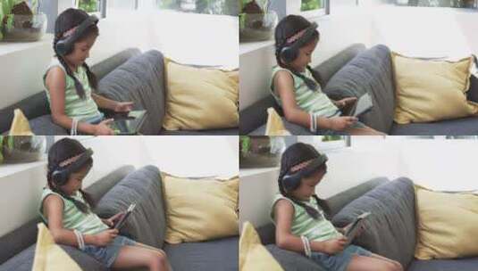 戴耳机的出生女孩在沙发上使用平板电脑高清在线视频素材下载