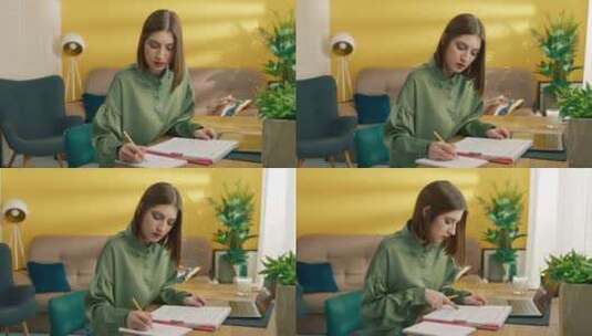 年轻漂亮的女学生坐在桌旁做笔记在家学习高清在线视频素材下载