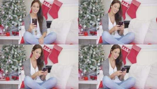 女孩在圣诞装饰前的沙发上玩手机高清在线视频素材下载