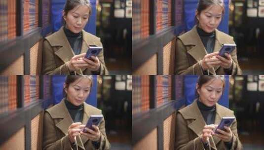 中年女性在书店书架前使用手机高清在线视频素材下载