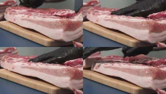 一个戴黑手套的男人在砧板上切猪肉。高清在线视频素材下载